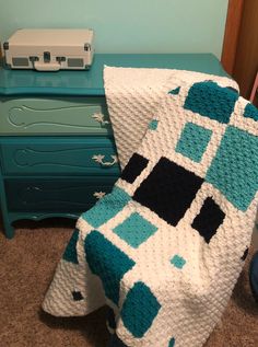 a blue and white crocheted blanket sitting on top of a bed next to a dresser