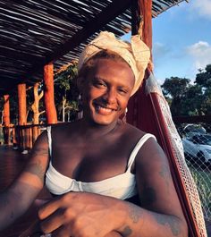 a woman sitting in a hammock smiling at the camera with tattoos on her arms