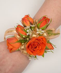 an orange wrist corsage with flowers and ribbons on it's arm,