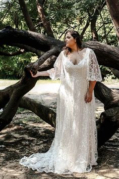 a woman in a white dress standing next to some trees and looking off into the distance