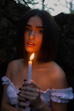 a woman holding a lit candle in her hand with the light shining on her face