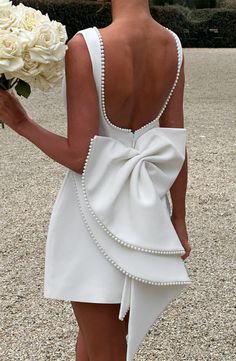 the back of a woman in a white dress holding a bouquet of flowers and looking down