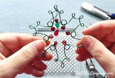 two hands are holding wire work together to make a snowflake ornament