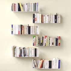 three white shelves with books on them against a wall