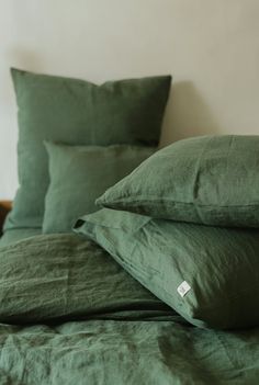 a bed with green linens and pillows on top of each other in front of a white wall