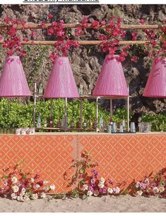 four pink lamps are hanging over a table with flowers and bottles on the wall behind them