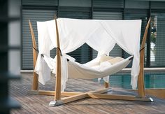 a hammock bed with white sheets and curtains on the side of a swimming pool