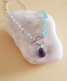 Three amazing crystals joined together into one fabulous necklace!On one side of necklace is a row of raw natural Apatite nuggets that are hand wire wrapped and joined to a dainty Moonstone beaded chain. A natural Amethyst teardrop hangs from the modern toggle clasp that completes this beautiful unique necklace.Details:* Raw natural Apatite nuggets Size about 12 mm* Natural beaded Moonstone Chain* Natural Bezel Set Amethyst Teardrop Size about 14 mm* Sterling Silver Wire* Toggle is Silver-Rhodiu Handmade Blue Amethyst Crystal Necklaces, Handmade Blue Amethyst Crystal Necklace, Spring Jewelry Trends, Amethyst Stone Necklace, Spring Jewelry, Moonstone Beads, Blue Apatite, Necklace Beaded, Unique Necklace