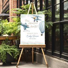 an easel with a sign that says the adventure awaits on it in front of a building