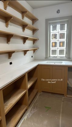 an empty kitchen with wooden shelves on the wall and a window in the back ground