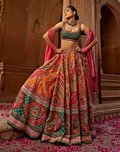 Aadhya lehenga set is an eye-catching piece crafted in multi-coloured festive colours printed silk, featuring heavy tassel strings with gota embroidery, hand adda work, and beads/sequins. The bold colours of pink, green and orange add a vibrant touch to this one-of-a-kind set. Multi Color Mehendi Outfit, Multicolor Lehenga Bridal, Carnival Indian Wedding Outfit, Orange Lengha Color Combos, Multi Colour Lehenga Indian Weddings, Traditional Nepali Clothing, Semi Traditional Outfits For Women, Pink Lehenga For Haldi, Bold Prints Fashion