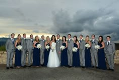 a group of people standing next to each other in front of a stone wall and cloudy sky