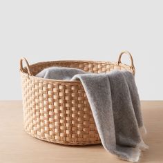 a woven basket with two gray blankets in it on a table next to a white wall