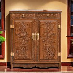 a wooden cabinet sitting in the middle of a room next to a potted plant