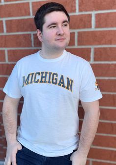 Support your Michigan Wolverines in this White Short Sleeve Fashion Tee! This Arch Fashion T Shirt features a screen printed wordmark `Michigan` with a Football Helmet on the arm. Be ready to shout "Go Michigan" when you wear this Michigan Short Sleeve Fashion T Shirt in the stadium or on the street. 100% ring-spun combed cotton with slub yarns, Super soft, natural texture, Distressed, vintage screen print, Arm hit printed logo on left sleeve, Premium, heathered design, High quality construction White Embroidered T-shirt For College, Collegiate Cotton T-shirt With Embroidered Graphics, College Fan Apparel T-shirt With Embroidered Graphics, Cotton Tops With Embroidered Graphics For Fan Gear, White Team Spirit T-shirt With Embroidered Graphics, Pre-shrunk Cotton Sports Fan T-shirt, Fan Apparel T-shirt With Embroidered Graphics And Crew Neck, Fan Apparel T-shirt With Embroidered Graphics, White School Spirit T-shirt With Embroidered Graphics