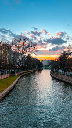 the sun is setting over a river with buildings on both sides