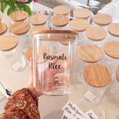 a person holding up a jar with labels on it and some flowers in the background