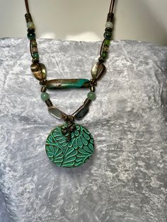 Fun, bold colorful 2" pendant with Palm Tree charm on two strands of 1mm bronze leather cord, Peacock Agate, Aventurine, India Agate and two 3/4" each Mother of Pearl. A large Genuine 1 1/2" Sea Green Turquoise Bead takes center stage bringing the colors together. Bronze toggle to close. Necklace is 22"  around neck with drop of pendant  total is 24". No lead or nickel used. Please use the Last On, First Off approach. Stones discolor with lotions, perfumes, hairspray, sweat, chlorine, even some soaps, and will break if dropped. Green Spiritual Necklace For Festivals, Green Spiritual Necklace For Festival, Bohemian Beaded Medallion Necklace, Green Multi-strand Spiritual Jewelry, Green Spiritual Multi-strand Jewelry, Adjustable Multi-strand Turquoise Necklace Gift, Bohemian Green Turquoise Necklace With Large Pendant, Green Bohemian Double Strand Jewelry, Bohemian Green Pendant Beaded Necklace