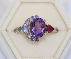 This Breathtaking One-of-a-kind ring Features a 2.6 carat 10 mm by 8 mm Amethyst. Flanked by Pink Sapphires, Blue Sapphire, Blue-Green Sapphires, Lavender-Purple Sapphire, Red Sapphire, Deep Pink Sapphires, Ruby, Yellow Citrine, Rubellite pear shape Tourmaline. All stones are 100% Natural and Ethically Sourced. Set in 14k Yellow Gold. Can be custom made in any gold color (pink, yellow or white). Choosing OOAK (one-of-a-kind) ring makes you the owner of something that nobody else has. A little wi Multicolor Oval Gemstones For Anniversary, Oval Multicolor Gemstones For Anniversary, Multicolor Oval Ruby Ring For Gift, Multicolor Oval Ruby Ring Gift, Multicolor Oval Amethyst Ring With Gemstone Accents, Multicolor Oval Amethyst Ring With Accent Stones, Multicolor Amethyst Rings With Accent Stones, Multicolor Amethyst Gemstone Ring, Multicolor Oval Amethyst Gemstone Ring