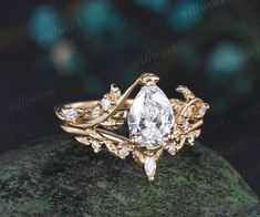 a gold ring with a pear shaped diamond surrounded by leaves on top of a rock