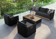 an outdoor living room with black furniture and trees in the backgroung area