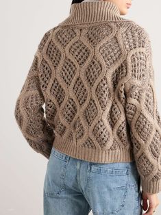 a woman wearing a brown sweater and jeans is looking down at the back of her jacket