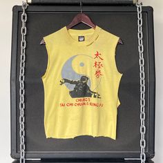 "VINTAGE :: 80s / 90s Kung Fu Cut Off Tank Tee COLOUR :: Yellow  FIT/TAG :: XS-S MATERIAL :: Cotton / Poly CONDITION :: Good MEASUREMENTS :: Armpit to Armpit Width - 43cm // 17\"   Total Length CB Neck to Bottom - 53.5cm // 21\"    DETAILS :: Great condition 80s/90s cut off tank tee. Screen Stars tag. Front print only. Well worn, super soft, cut down armhole / sleeves. Side cut drop approx 14\". Print is cracked & faded, marks, holes & tears but all adds to the t-shirts character :) Small red/ pink stains seen on front. Unisex cutoff XS-S. NOTE :: Each hand selected vintage or preloved piece is a one-of-a-kind item & can only be purchased by a single customer. Measurements are in cm/inches lying flat (double width for circumference). Any major details, features or flaws will be described o Vintage Sleeveless T-shirt With Graphic Print, Vintage Sleeveless Tops With Screen Print, Vintage Fitted Tops For Streetwear, Vintage Yellow Tops With Screen Print, Vintage Yellow Top With Screen Print, Vintage Sleeveless Graphic Print T-shirt, Vintage Fitted T-shirt For Streetwear, Fitted Vintage T-shirt For Streetwear, Retro Vintage Print Tops For Streetwear