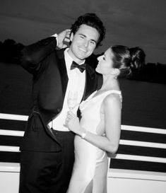 a man in a tuxedo standing next to a woman holding a wine glass