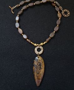 "One of a kind petrified wood pendant sourced in Nevada adorns this 18\" necklace with quart, bronze and brass elements.  The stone is just over 2\" in length and hangs approx. 3\" down from base of the necklace." Artisan Brown Necklace With Oval Pendant, Brown Brass Necklace For Healing, Unique Jasper Gold Necklace, Artisan Jasper Gold Necklace, Unique Gold Jasper Necklace, Brown Agate Amulet Necklace, Earthy Agate Gold Necklace, Unique Jasper Necklace With Large Pendant, Rustic Brown One-of-a-kind Necklace