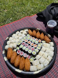 a plate with sushi and rolls on it sitting on a blanket next to a drink