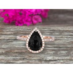 a pear shaped black and white diamond ring on top of a piece of wood with pink flowers in the background