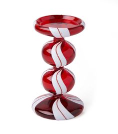 a red and white striped glass vase sitting on top of a wooden stand in front of a white background