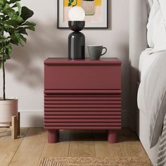 a nightstand with a coffee cup on it next to a painting and potted plant