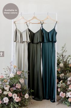 three bridesmaid dresses hanging in front of flowers