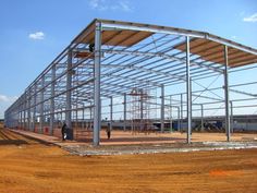 a large metal building under construction in the middle of an open field with people walking around it