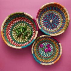 three woven baskets on a pink surface with one green plant in the middle and two red ones