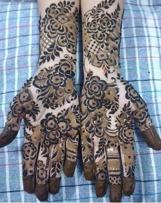 two hands that are decorated with henna on top of a bed and plaid blanket