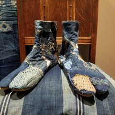 two pairs of dirty shoes sitting on top of a blue striped pillow in front of a wooden chair