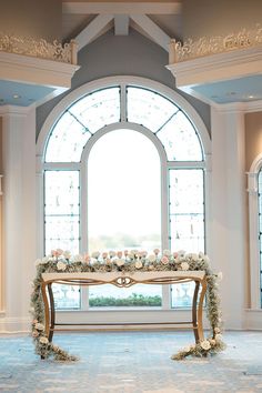 a table with flowers and greenery in front of a large window at a wedding