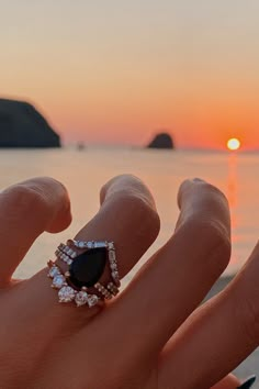 a woman's hand with a ring on it and the sun setting in the background