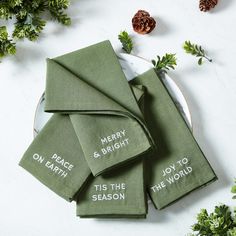 four green napkins with merry and bright words on them sitting on a white plate