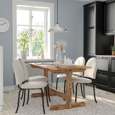 a dining room table with white chairs and a clock on the wall above it in front of a window