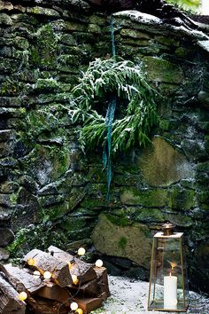 a wreath hanging from the side of a stone wall next to a lantern with candles on it