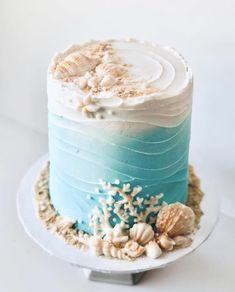 a blue and white cake with sea shells on top is sitting on a platter