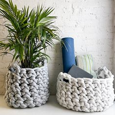 two knitted baskets sitting next to each other on a table with a potted plant