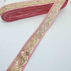 a pink and gold ribbon on a white surface with other items in the back ground