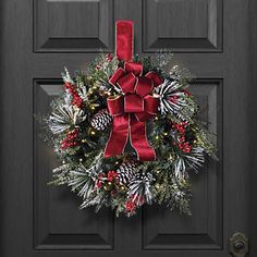 a black door with a red bow and pineconis wreath on it's side