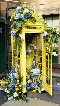 a yellow phone booth covered in flowers and greenery