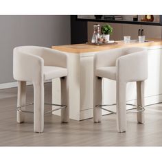 two white stools sitting in front of a counter with a wooden table and chairs