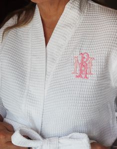 a woman wearing a white robe with pink monogrammed initials